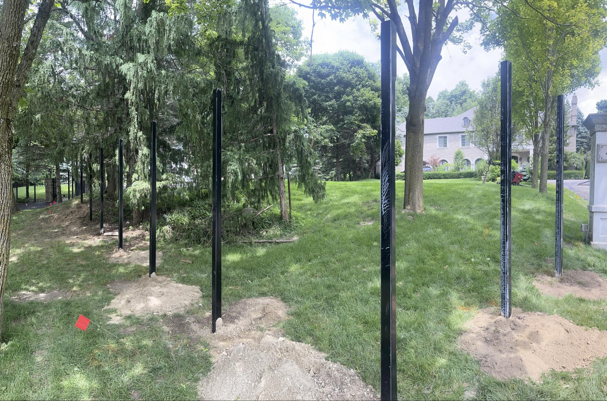 Metal fence posts pounded into ground installation Black metal fence posts driven into ground along property line in residential yard